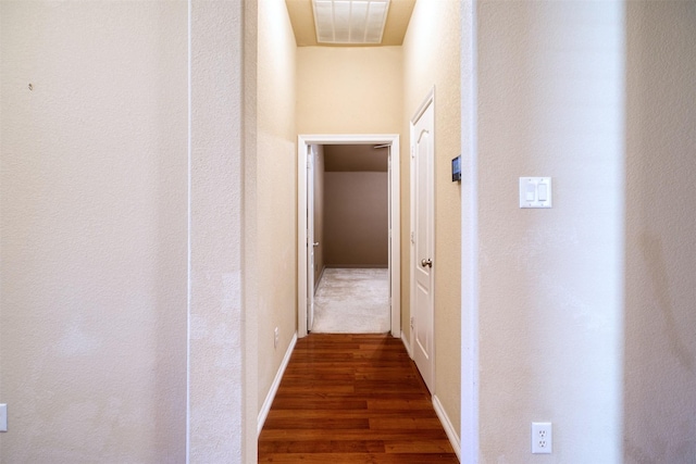 hallway with wood finished floors, visible vents, and baseboards