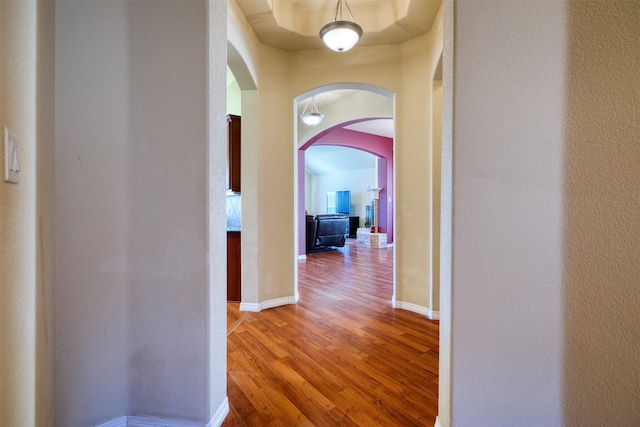 hall with arched walkways, a textured wall, baseboards, and wood finished floors