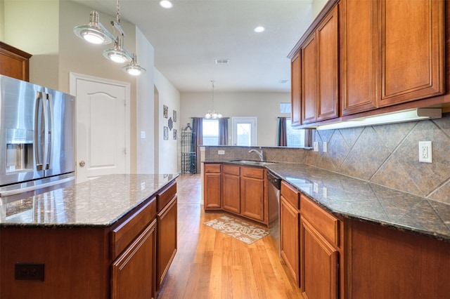 kitchen with brown cabinetry, light wood-style flooring, a sink, stainless steel appliances, and backsplash