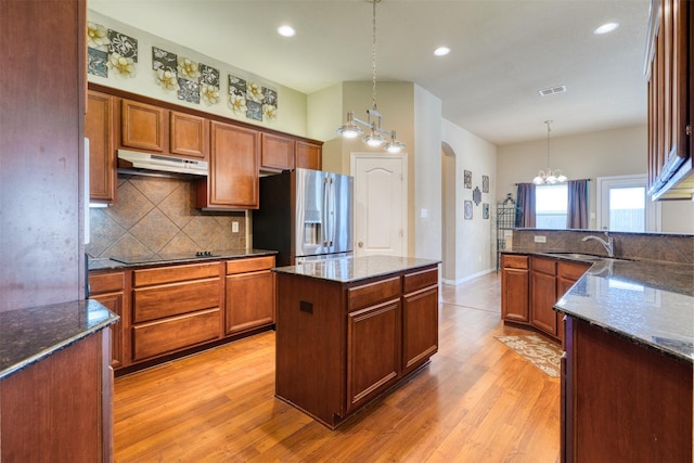 kitchen featuring black electric stovetop, under cabinet range hood, a sink, visible vents, and stainless steel refrigerator with ice dispenser