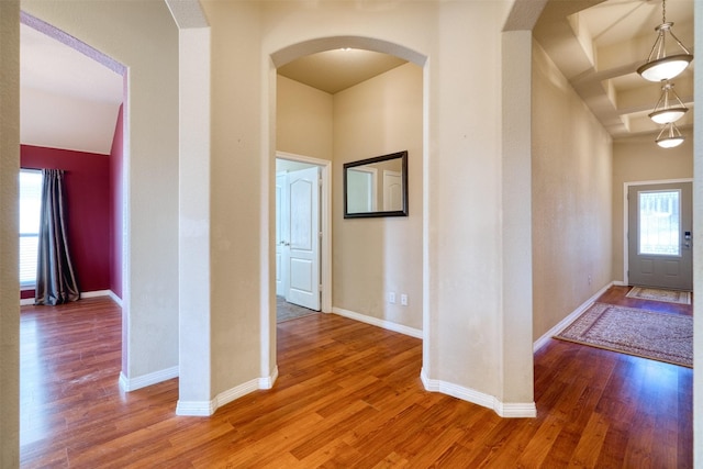 corridor with arched walkways, baseboards, and wood finished floors