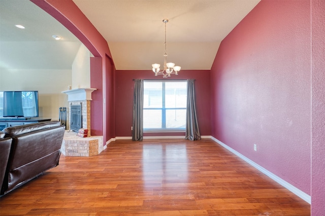 living room featuring lofted ceiling, an inviting chandelier, a brick fireplace, wood finished floors, and baseboards