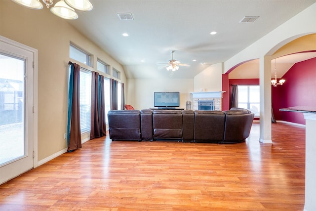 living area with vaulted ceiling, a stone fireplace, light wood finished floors, and baseboards