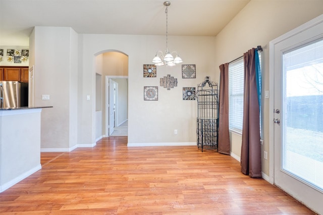 unfurnished dining area featuring arched walkways, light wood finished floors, a notable chandelier, and baseboards