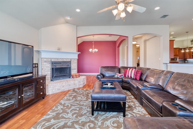 living area featuring arched walkways, a fireplace, visible vents, light wood-style floors, and vaulted ceiling