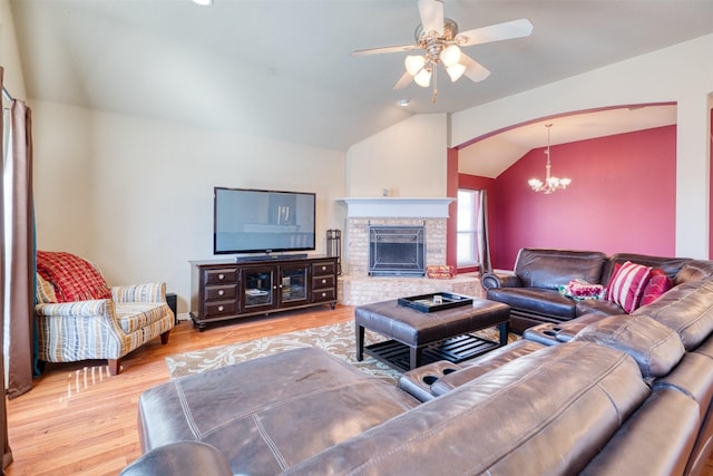 living area with arched walkways, lofted ceiling, a fireplace with raised hearth, wood finished floors, and ceiling fan with notable chandelier