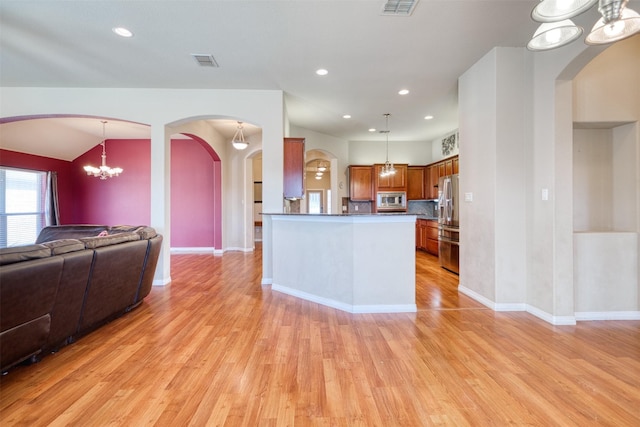 kitchen with visible vents, light wood-style floors, open floor plan, appliances with stainless steel finishes, and brown cabinets