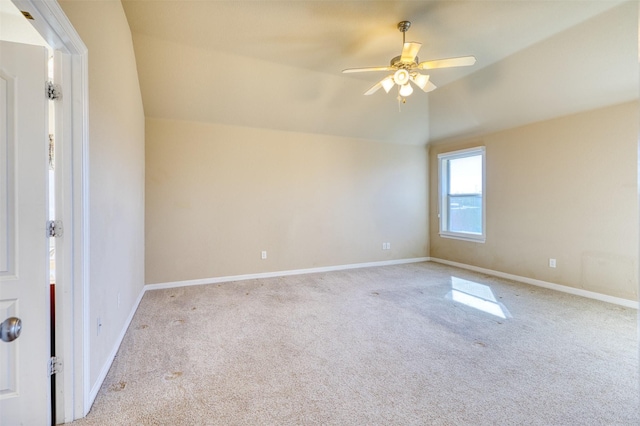 carpeted empty room with a ceiling fan, vaulted ceiling, and baseboards