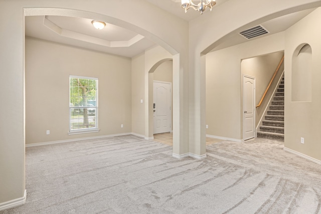 empty room with baseboards, visible vents, a raised ceiling, light colored carpet, and an inviting chandelier