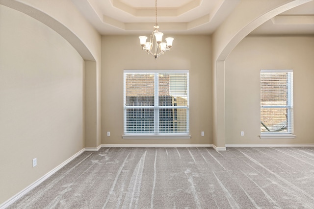 spare room with a high ceiling, carpet flooring, baseboards, a raised ceiling, and an inviting chandelier