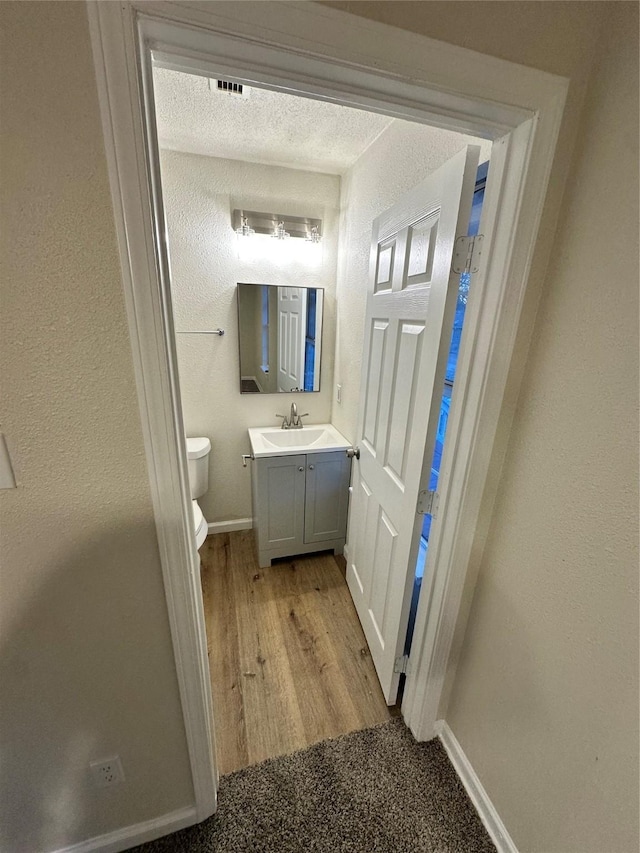 bathroom featuring toilet, a textured wall, wood finished floors, and vanity