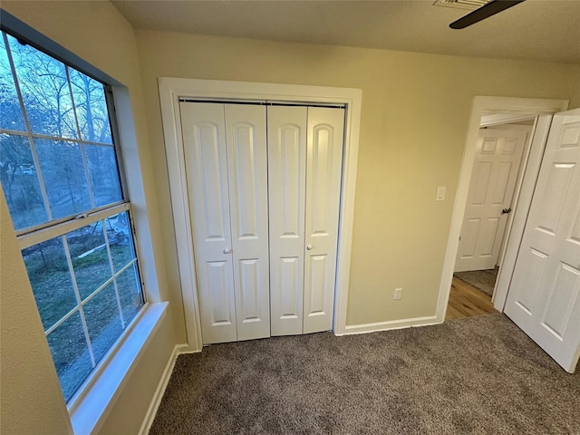 unfurnished bedroom featuring ceiling fan, baseboards, dark colored carpet, and a closet