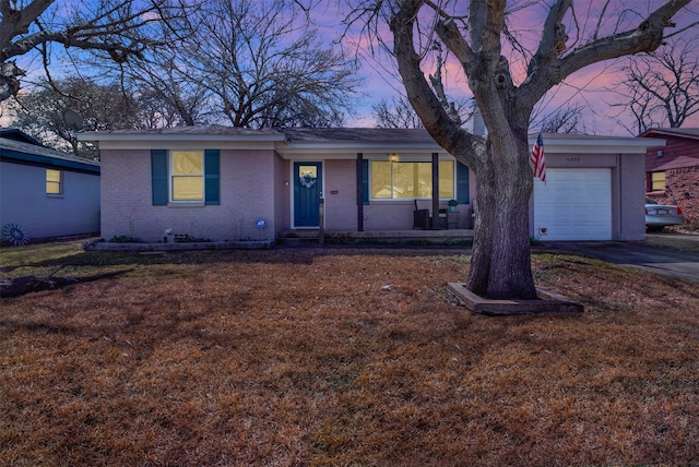 single story home featuring a porch, an attached garage, brick siding, driveway, and a front yard