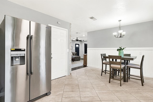 dining area with light tile patterned floors, a wainscoted wall, visible vents, and ceiling fan with notable chandelier