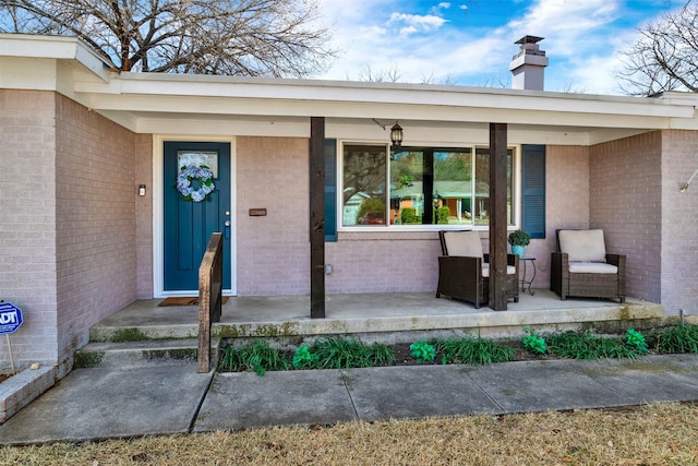 view of exterior entry featuring covered porch, brick siding, and a chimney