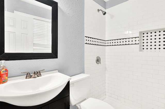 bathroom featuring a textured wall, vanity, a tile shower, and toilet