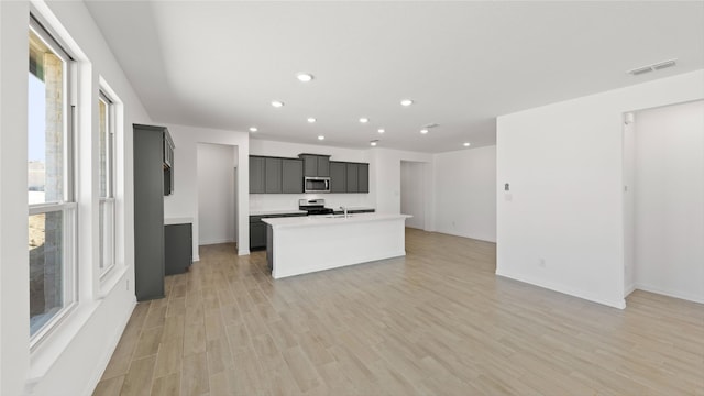 kitchen featuring visible vents, light wood-style floors, light countertops, appliances with stainless steel finishes, and an island with sink