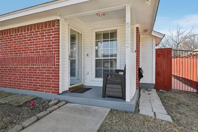 property entrance featuring brick siding, a porch, and fence