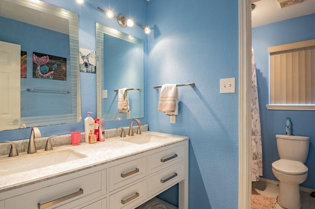 bathroom featuring visible vents, double vanity, a sink, and toilet