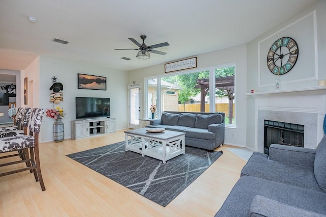 living area featuring light wood-style flooring, a fireplace, visible vents, and ceiling fan