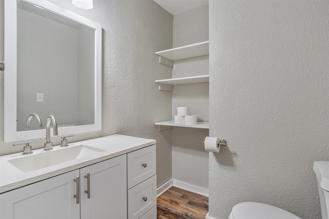 half bathroom with a textured wall, toilet, wood finished floors, vanity, and baseboards