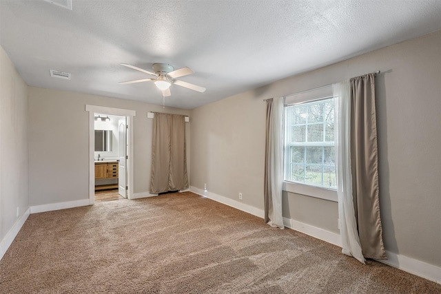 unfurnished bedroom featuring baseboards, visible vents, ensuite bathroom, a textured ceiling, and carpet floors