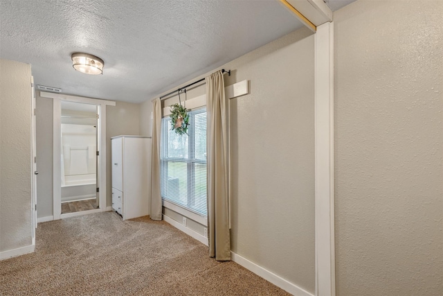 empty room with a textured ceiling, a textured wall, carpet, and baseboards