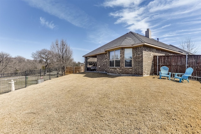 view of side of home with brick siding, a yard, a chimney, a shingled roof, and a fenced backyard