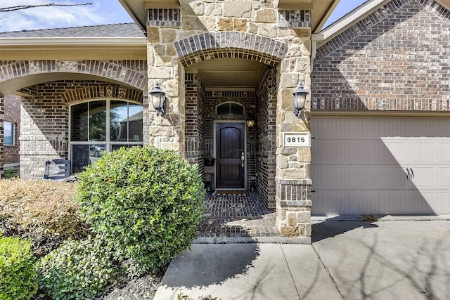 entrance to property with a garage, stone siding, a shingled roof, and brick siding