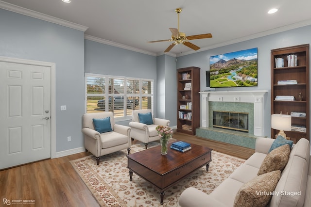 living room with ornamental molding, a high end fireplace, ceiling fan, wood finished floors, and baseboards