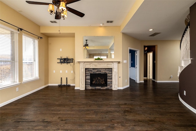 unfurnished living room with visible vents, a stone fireplace, ceiling fan, and dark wood-style flooring