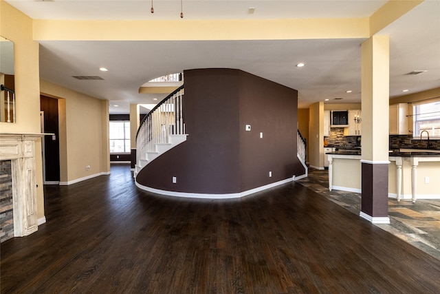 unfurnished living room featuring a healthy amount of sunlight, dark wood finished floors, and stairs