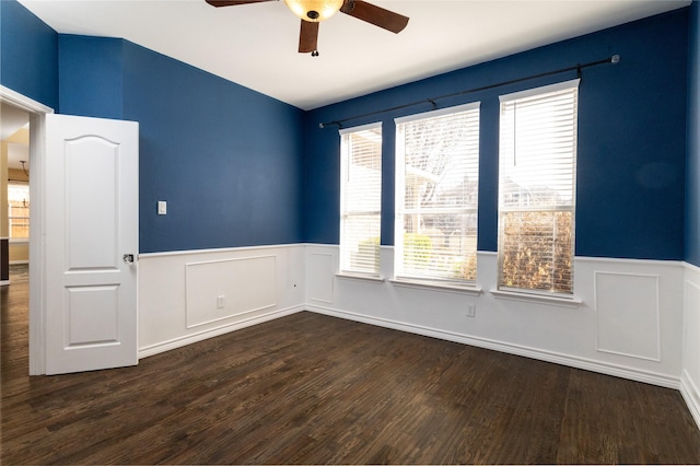 empty room with dark wood-type flooring, a ceiling fan, and wainscoting