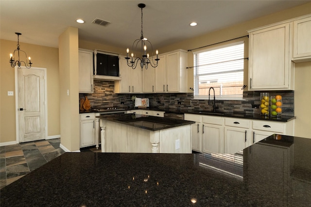 kitchen featuring visible vents, a sink, dark stone countertops, backsplash, and an inviting chandelier