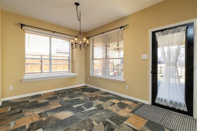 unfurnished dining area with a chandelier, stone finish flooring, and baseboards