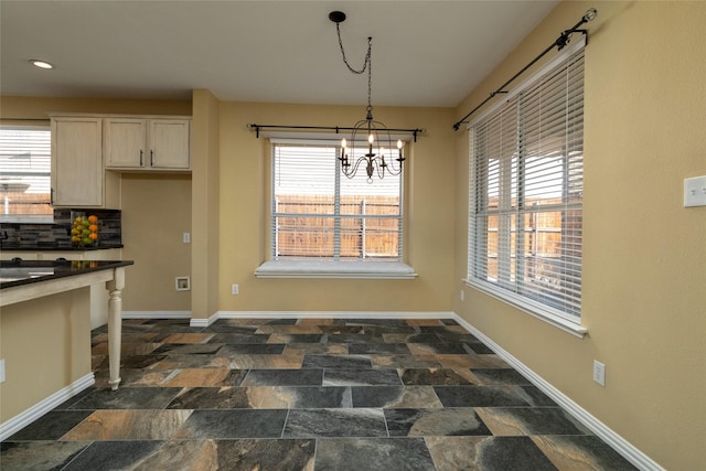 dining space with stone finish floor, a notable chandelier, a healthy amount of sunlight, and baseboards