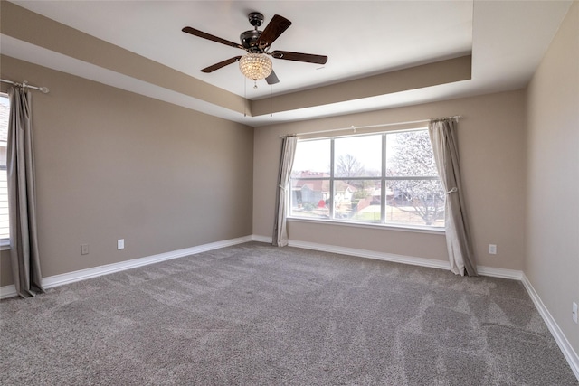 unfurnished room with a tray ceiling, baseboards, carpet, and a ceiling fan