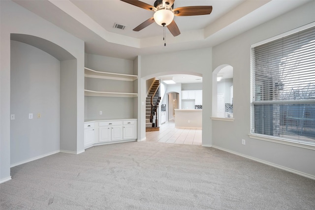 spare room with baseboards, visible vents, arched walkways, light colored carpet, and a tray ceiling