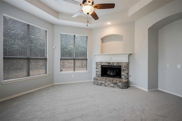 unfurnished living room featuring a fireplace, a raised ceiling, carpet flooring, ceiling fan, and baseboards