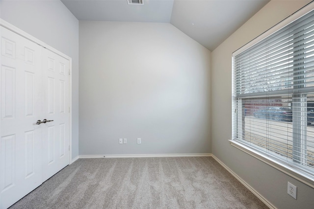 empty room with vaulted ceiling, carpet, visible vents, and baseboards