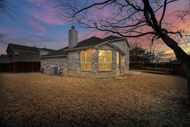 back of property at dusk with a fenced backyard, central air condition unit, brick siding, a yard, and a trampoline