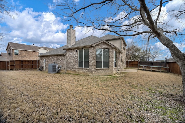 back of property with a trampoline, brick siding, a lawn, central AC, and a fenced backyard