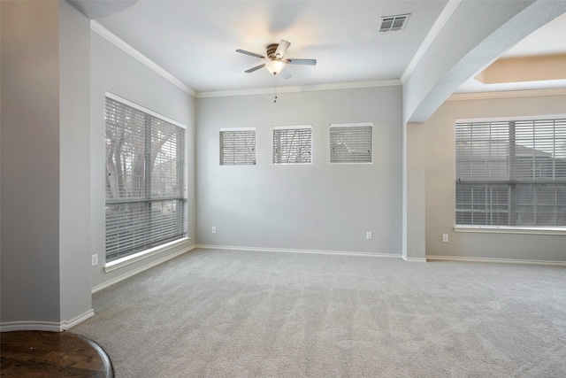 carpeted spare room featuring baseboards, visible vents, a ceiling fan, arched walkways, and crown molding