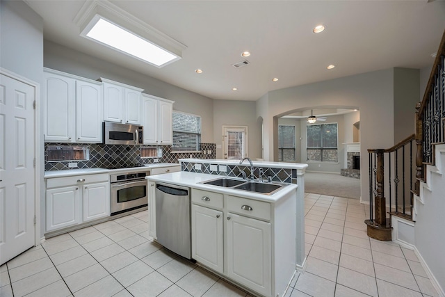 kitchen featuring a fireplace with raised hearth, a sink, visible vents, appliances with stainless steel finishes, and an island with sink