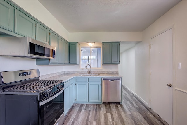 kitchen with light stone counters, light wood-style flooring, stainless steel appliances, a sink, and green cabinetry