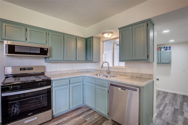 kitchen featuring light wood finished floors, stainless steel appliances, a sink, light stone countertops, and baseboards