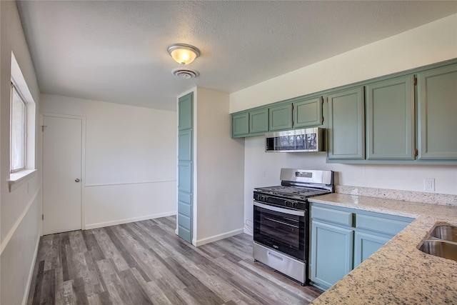 kitchen with stainless steel appliances, visible vents, a textured ceiling, wood finished floors, and baseboards