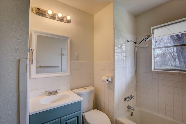 bathroom featuring a wainscoted wall, tile walls, bathtub / shower combination, toilet, and vanity