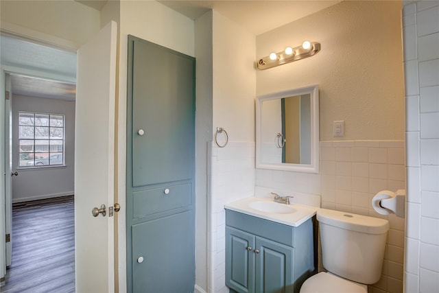 bathroom featuring toilet, wainscoting, tile walls, and vanity