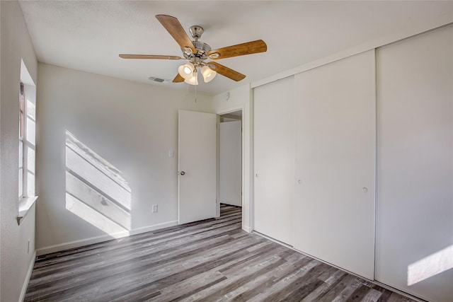 unfurnished bedroom featuring a closet, visible vents, a ceiling fan, wood finished floors, and baseboards